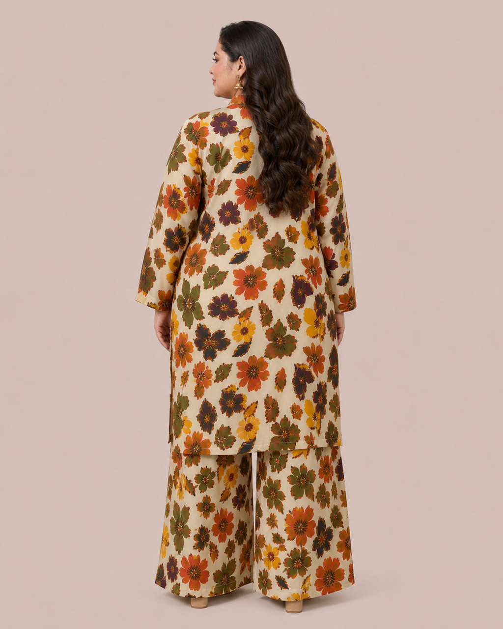 A woman shown from the back wearing a cream-colored two-piece kurta set with a dense, colorful floral pattern in orange, yellow, green, and brown, set against a solid beige studio background.