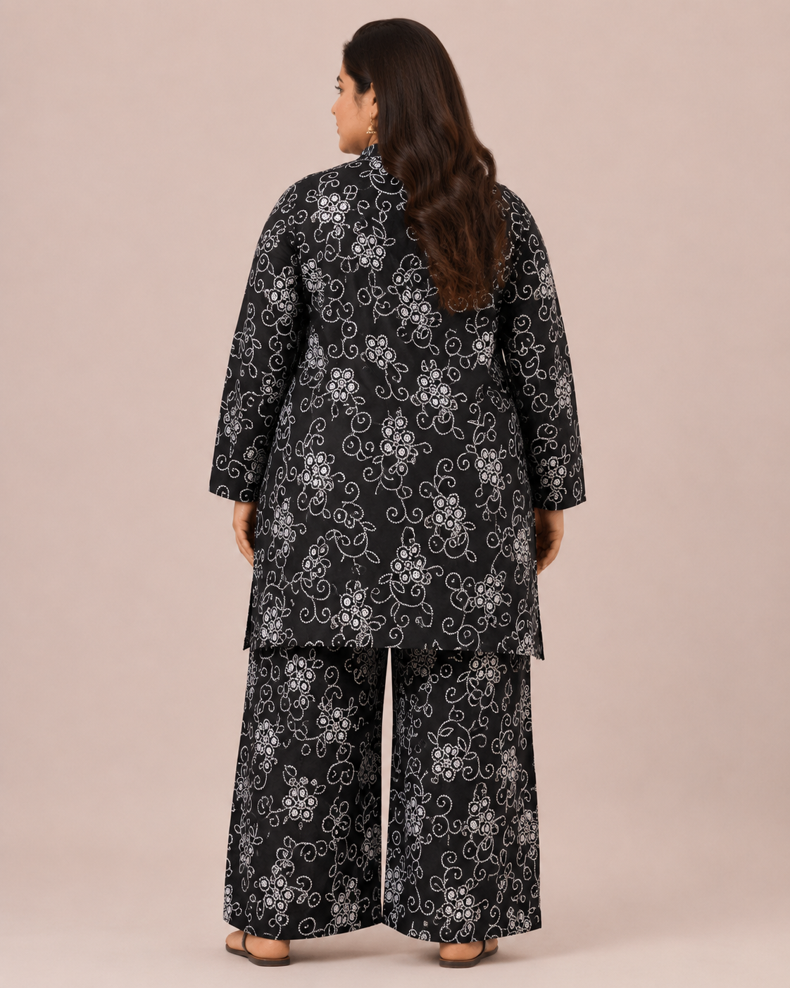 Back view of a smiling plus-size model posing in a matching black and white floral vine printed cotton lawn kurta and wide trouser co-ord set.