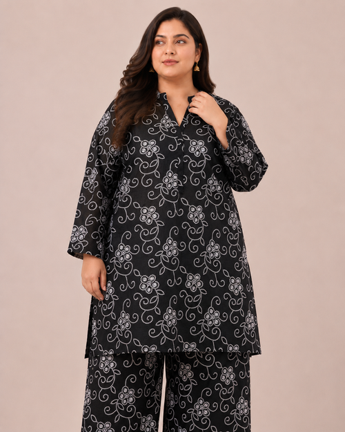 Front view of a smiling plus-size model posing in a matching black and white floral vine printed cotton lawn kurta and wide trouser co-ord set.