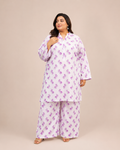 Front view of a smiling plus-size model posing in a matching white and lavender leaf printed cotton lawn kurta and wide trouser co-ord set.