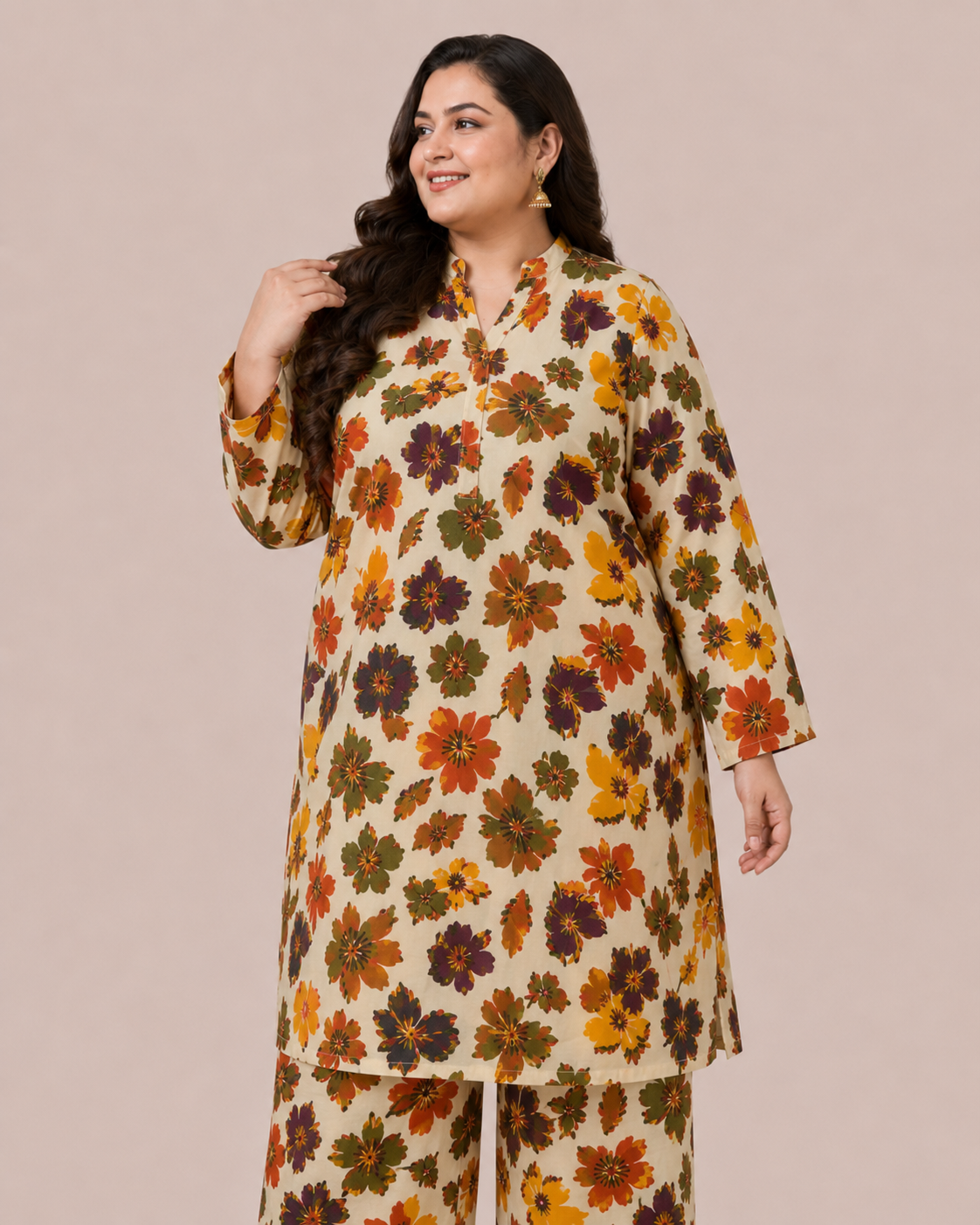 A woman modeling a matching two-piece kurta and trouser set with a beige base and a colorful floral print in orange, yellow, green, and brown, set against a solid beige studio background.